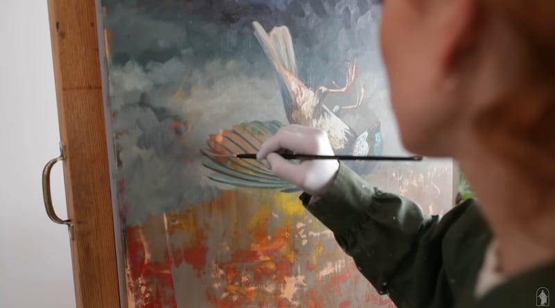 Jenedy Paige working on her painting of a sparrow falling into waiting hands.