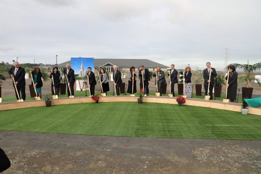 A row of people in Sunday best holding ceremonial golden shovels with a scoop of dirt.