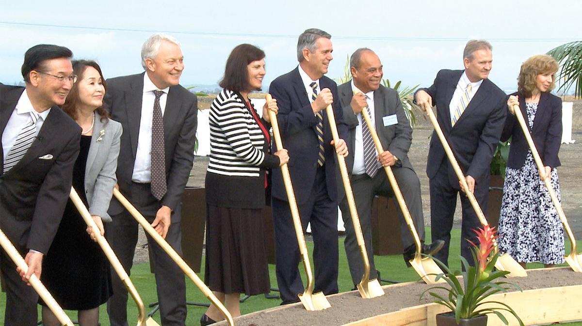 A row of people in Sunday best holding ceremonial golden shovels and smiling.