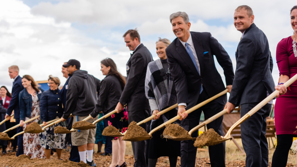 A row of people in Sunday best holding ceremonial golden shovels with a scoop of dirt.