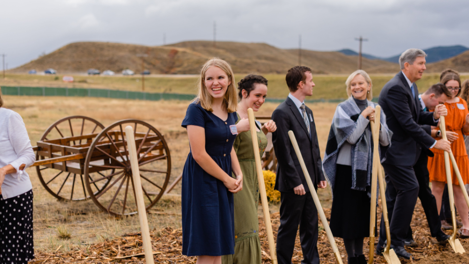 A row of people in Sunday best holding ceremonial golden shovels into the ground.