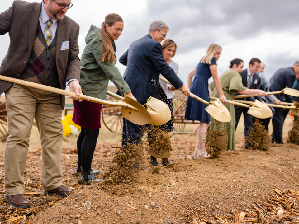 A row of people in Sunday best holding ceremonial golden shovels with a scoop of dirt.