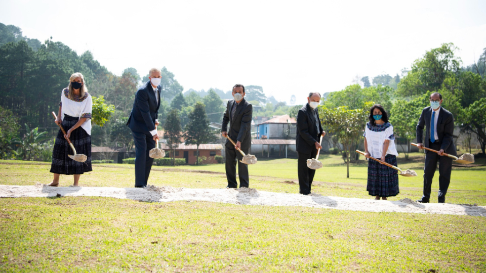 A row of people in Sunday best holding ceremonial golden shovels with a scoop of dirt.