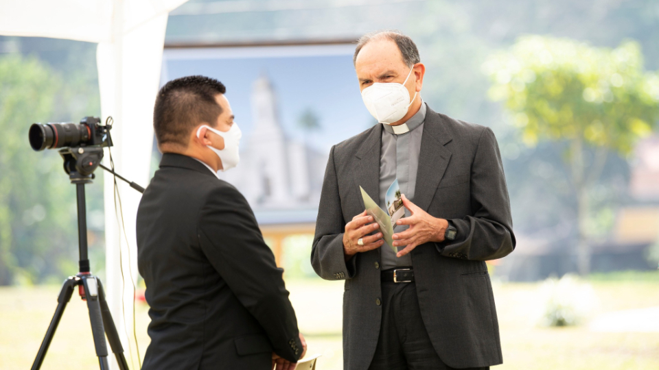 Two men standing and talking to each other, both wearing a suit coat and face mask.