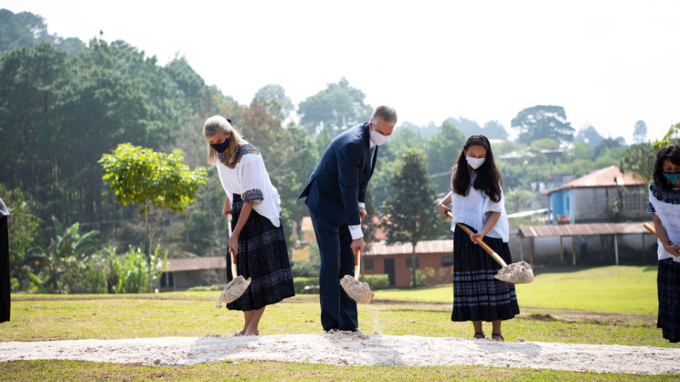 One man in a suit and two women in dresses holding ceremonial golden shovels with a scoop of dirt in them.