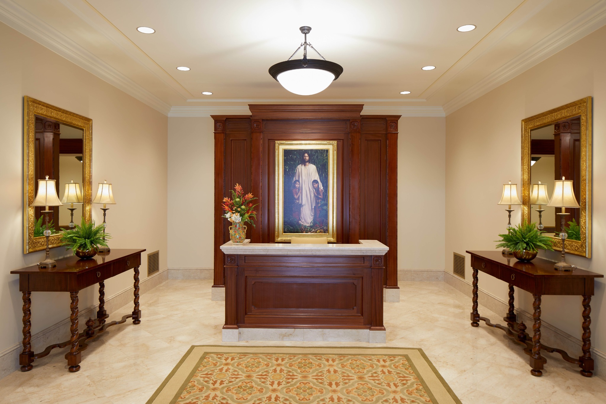 A dark-wood desk in front of a painting of Jesus in a rectangular frame.