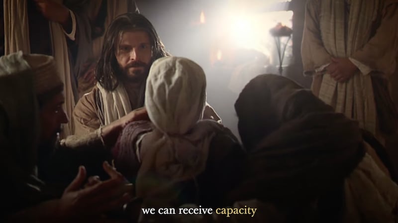 An actor portraying the Savior ministers to a woman in a crowd whose back is to the camera.